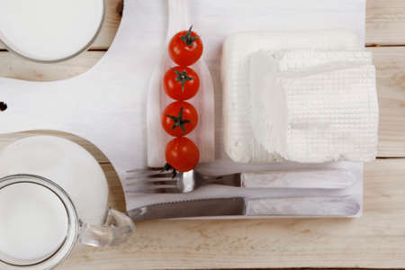 healthy dairy food fresh white greek goat sheep feta cheese on plate with milk in glass and full jug cherry tomatoes french bun over light wooden table with cutleryの写真素材