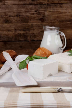 dairy food fresh white greek goat sheep feta cheese on plate with milk in pitcher cherry tomatoes french bun over dark wooden tableの写真素材