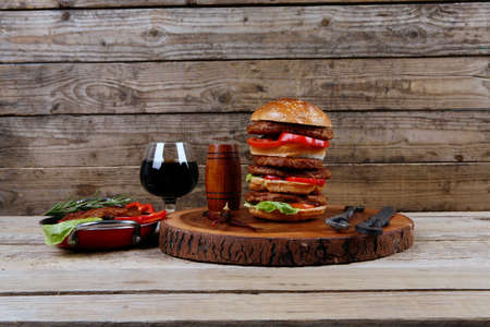 fresh grilled beef huge hamburger served on wood plate with red wine glass chili pepper rosemary green salad leaf and forged vintage antique cutlery over wooden table empty space for textの写真素材