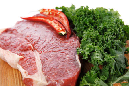 fresh raw beef meat fillet with red hot chili pepper and raw kale leafs on wooden board isolated over white backgroundの写真素材