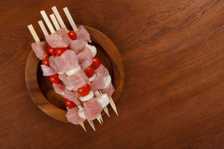 fresh raw meat fillet shish kebab turkey pork pink on skewers tomatoes mushrooms on wooden dish on big wood tableの写真素材