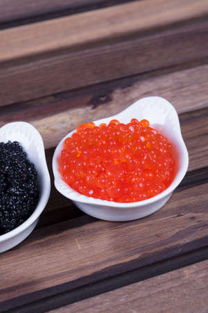 black sturgeon hausen caviar with red salmon caviar in white bowls on wooden backgroundの写真素材