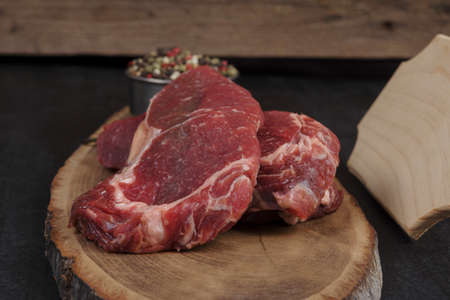 fresh raw beef piece fillet on middle size wooden plate with pepper and peppercorns in measuring spoon with name plate space for text on black backgroundの写真素材
