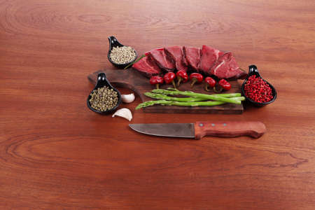 fresh beef meat asparagus greenery spices cutlery wooden table pepper crushed hot chili vegetables bowl served garlic cutting boardの写真素材