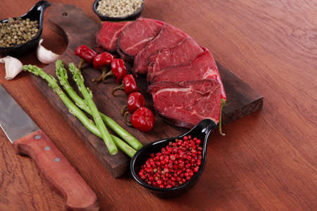 fresh beef meat asparagus greenery spices cutlery wooden table pepper crushed hot chili vegetables bowl served garlic cutting boardの写真素材