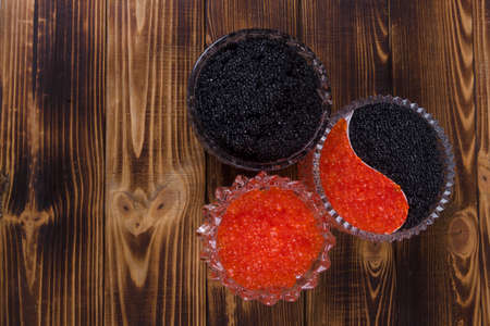 fresh raw red salmon caviar with black sturgeon caviar in white crystal bowls on burned vintage wooden table backgroundの写真素材