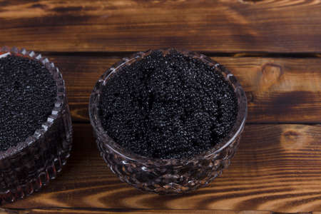 fresh raw red salmon caviar with black sturgeon caviar in white crystal bowls on burned vintage wooden table backgroundの写真素材