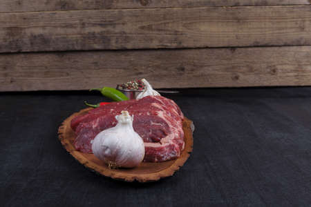 fresh raw beef pieces fillet on big size wooden plate with pepper and peppercorns in measuring spoon space for text on black backgroundの写真素材