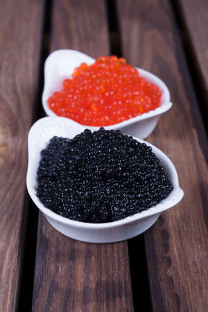 black sturgeon hausen caviar with red salmon caviar in white bowls on wooden backgroundの写真素材