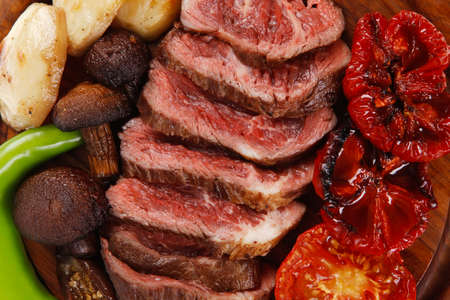fresh grilled bbq beef meat rib eye steak on wooden plate with baked tomatoes mushroom, potatoes, hot chili pepper isolated on white backgrodunの写真素材