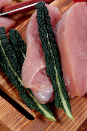 fresh raw turkey meat steak fillet with vegetables kale tomatoes lettuce red hot chili pepper and dark olives on cutting board over wooden tableの写真素材