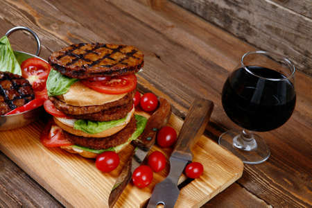 fresh grilled beef double huge hamburger served on wooden plate with wine cherry tomatoes and rosemary over tableの写真素材