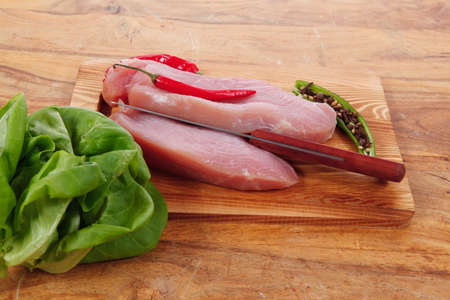 fresh raw turkey steak fillet with red hot chili pepper and green salad on cutting board over wooden tableの写真素材