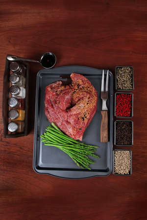 meat raw beef fillet chunk on black tray asparagus on wooden table allspice pink white black green peppercornの写真素材