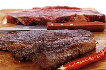 grilled and raw beef steak fillet meat with knife on wooden board isolated over white backgroundの写真素材