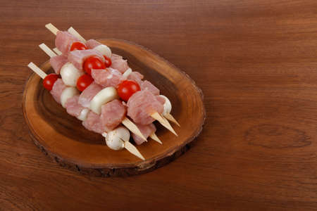 fresh raw meat fillet shish kebab turkey pork pink on skewers tomatoes mushrooms on wooden kitchen plate over wood tableの写真素材
