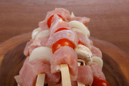 fresh raw meat fillet shish kebab turkey pork pink on skewers tomatoes mushrooms on wooden kitchen plate over wood tableの写真素材