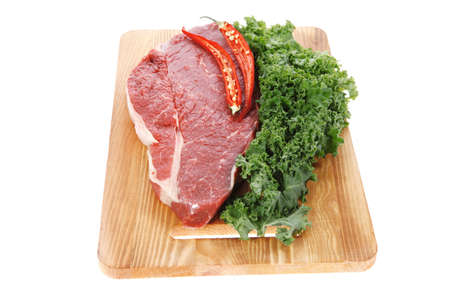 fresh raw beef meat fillet with red hot chili pepper and raw kale leafs on wooden board isolated over white backgroundの写真素材