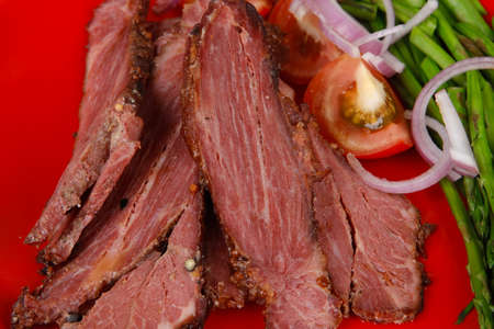fresh sliced roast beef on red plate with tomatoes and asparagus isolated on white backgroundの写真素材