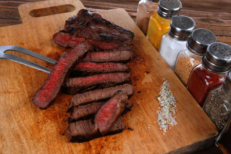grilled beef fillet steak on fork over wooden board served with different kind of dry spices salt crushed black pepper hot baked sweet paprika red hot chili on dark tableの写真素材