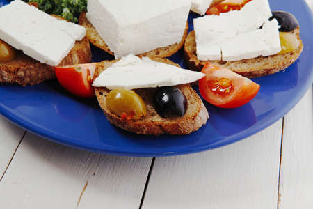 white feta greek cheese sandwich rye bread on blue plate with black spain olives tomatoes and cutlery over retro wooden tableの写真素材