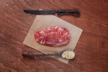 fresh raw beef rib eye steak on walnut table with salt spice and black iron antique forged cutlery fork knife empty space for textの写真素材