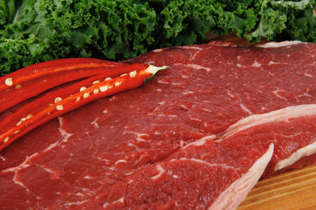 fresh raw beef meat fillet with red hot chili pepper and raw kale leafs on wooden board isolated over white backgroundの写真素材