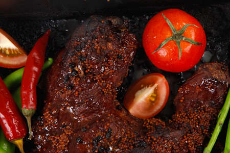 fresh glazed baked big beef meat rib chunk under sweet sauce with tomatoes hot chili pepper pink peppercorn and asparagus in black tray isolated on white backgroundの写真素材