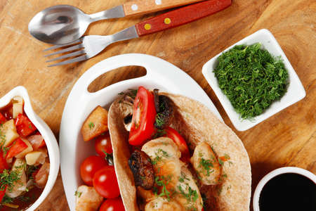 big mexican taco served with soup, fresh vegetables , baked mushroom with teriyaki sauce , on white crockery plates over wooden table with green staffの写真素材