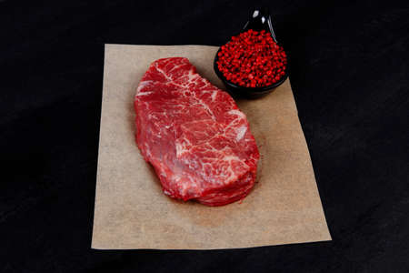 fresh raw beef meat marble steak on paper with saucer full pink peppercorn spice over black wooden tableの写真素材