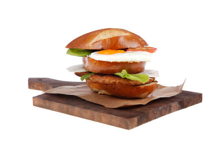 junk food big beef hamburger fried eggs on dark wood plate with modern cutlery isolated over white backgroundの写真素材
