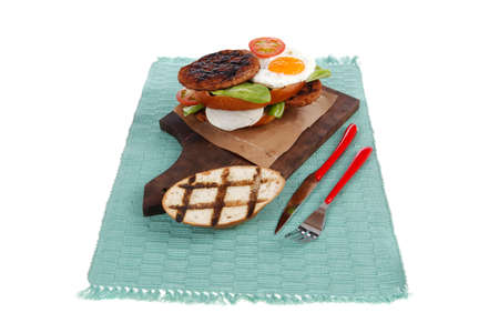 junk food big beef hamburger on dark wood plate with modern cutlery on blue mat isolated over white backgroundの写真素材