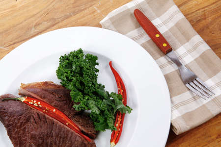 grilled beef steak fillet meat with red hot pepper and  raw kale leaf with ketchup sauce served on white plate over wood tableの写真素材
