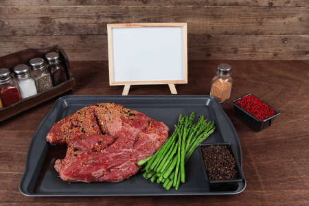 meat raw beef fillet chunk on black tray asparagus on wooden plate allspice pink peppercorn mustard nametable  empty space for textの写真素材