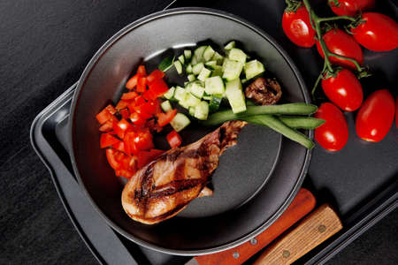 fresh hot grilled turkey drumstick leg with vegetables on black metal plate over wooden tableの写真素材