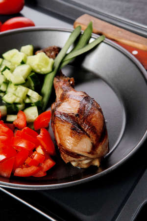 fresh hot grilled turkey drumstick leg with vegetables on black metal plate over wooden tableの写真素材