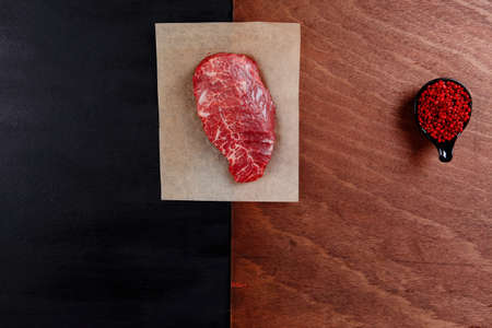fresh raw beef rib eye steak on black walnut wooden table with red hot pepper spice in saucerの写真素材