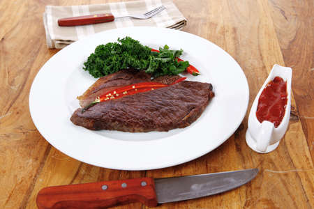 grilled beef steak fillet meat with red hot pepper and  raw kale leaf with ketchup sauce served on white plate over wood tableの写真素材