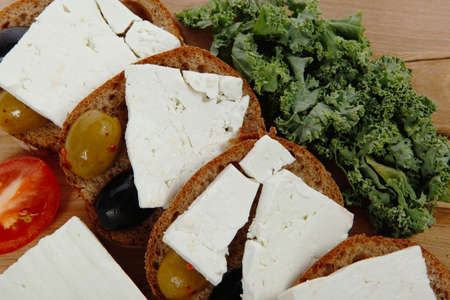 fresh greek feta cheese sandwich on wooden plate with hot green olives and black, goat cube, tomatoes kale over tableの写真素材