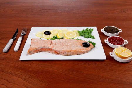 healthy food fresh roast red fish salmon with kale lemon antipesto ketchup sauce on white plate over wooden tableの写真素材