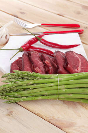 fresh beef meat slices asparagus spices cutlery wooden table pepper hot chili vegetables served garlic light cutting board ready to cookの写真素材