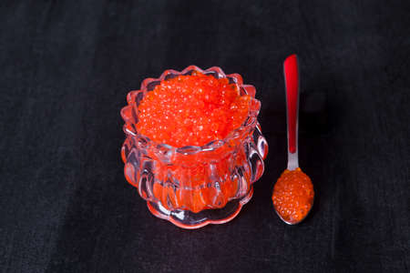 fresh raw red salmon caviar in white crystal bowls with small spoon on blackwooden backgroundの写真素材