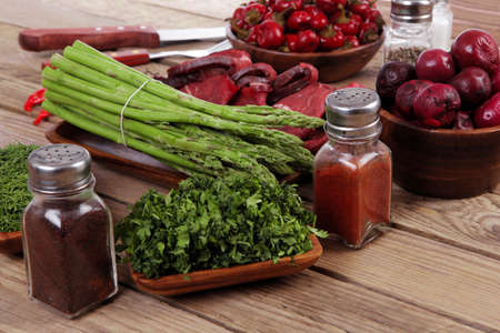 fresh beef meat asparagus greenery spices cutlery wooden table pepper crushed hot chili vegetables bowl servedの写真素材