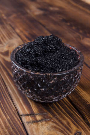 fresh raw red salmon caviar with black sturgeon caviar in white crystal bowls on burned vintage wooden table backgroundの写真素材