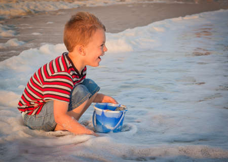 young boy playing at the beach in the surf with a pail.の写真素材