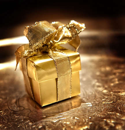 Image of a small gold giftwrapped box with ribbon on a silver trayの写真素材