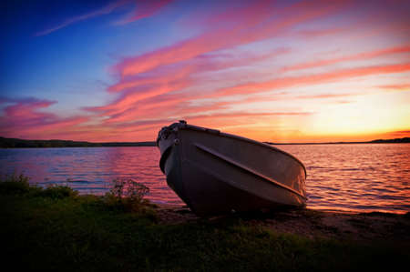 Fishing boat pulled up onto shore of a lake at sunsetの写真素材