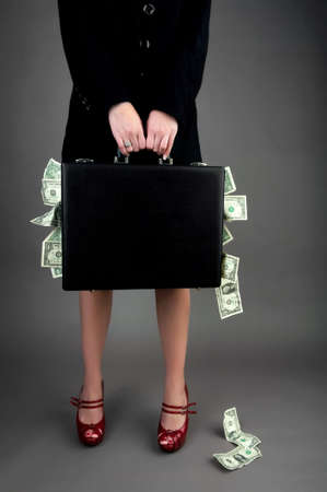 Image of a woman, from shoulders down, holding a black briefcase overflowing with moneyの写真素材