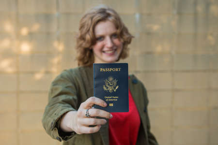 Smiling girl holding passport with arm extended towards cameraの写真素材