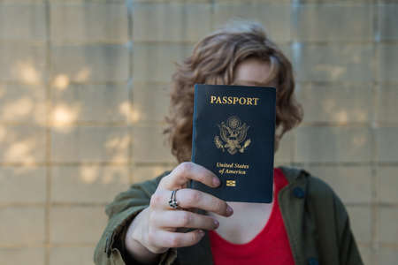 Girl holding passport, covering face, with arm extended towards cameraの写真素材